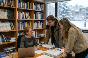 Usmiechnieta profesor rozmawia z parą studentów w soim gabinecie. Za oknem zimowy krajobraz.